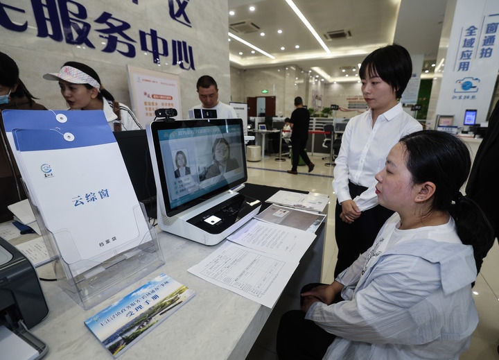 在浙江省嘉興市秀洲區(qū)王江涇鎮(zhèn)便民服務(wù)中心的“跨域通辦·云綜窗”窗口，辦理開(kāi)業(yè)登記的個(gè)體工商戶(hù)（右一）通過(guò)該系統(tǒng)與江蘇省蘇州市吳江區(qū)盛澤鎮(zhèn)行政審批局工作人員視頻連線(xiàn)，進(jìn)行身份讀取及材料線(xiàn)上審核（2024年5月9日攝）。新華社記者 徐昱 攝