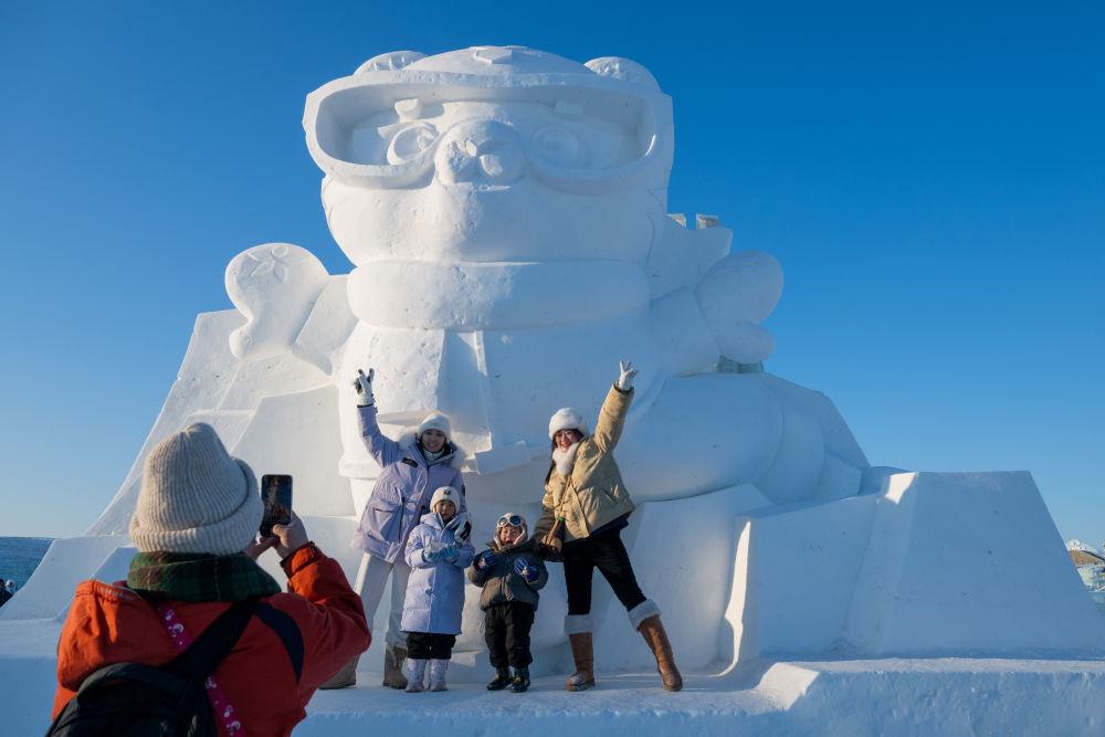 2025年1月3日，在黑龍江哈爾濱冰雪大世界園區(qū)，游客與亞冬會吉祥物雪雕“濱濱”合影